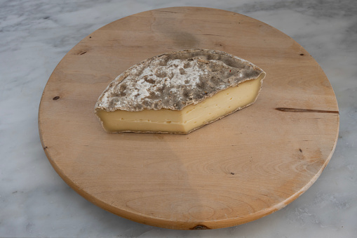 French culinary Still Life. Piece of cheese Tomme de Savoie placed on a wooden pan