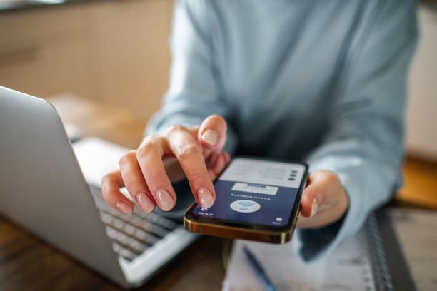 Young woman using a banking app on her phone while working from home