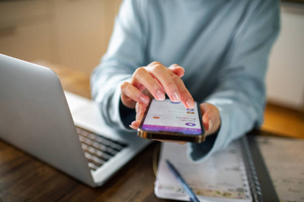 istock Young woman using a banking app on her phone while working from home 1479800431
