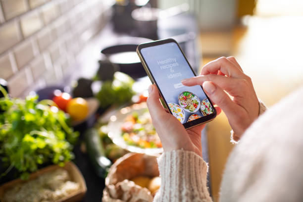 mulher adulta jovem usando um aplicativo de dieta em seu smartphone para preparar uma salada saudável - box lunch fotos - fotografias e filmes do acervo