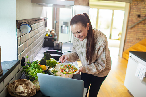 Close up of a Young adult woman preparing a healthy salad in the kitchen