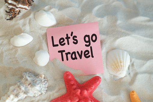 Let's Go Travel word on Paper is written on the beach sand