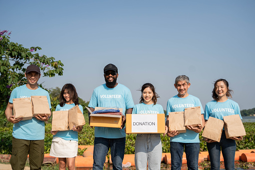 Team of volunteers holding donations boxes in outdoor. Volunteers putting food and shirt in donation boxes, social worker making notes charity