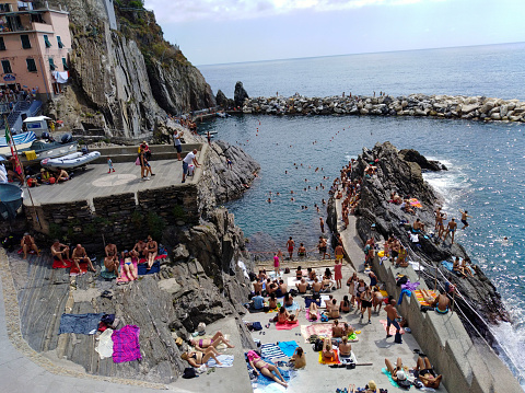 High angle view of the fishing harbour of Manarola full of tourists swimming in summer, Liguria, Italy