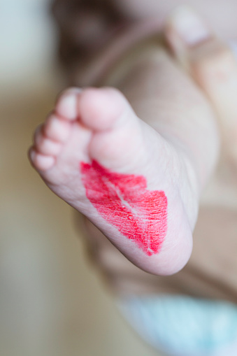 Foot of an unrecognizable baby with red lipstickkiss