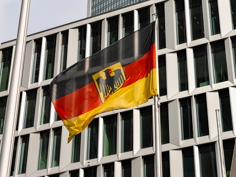 German flag in front of an office building exterior. The textile is waving in the wind. It is the symbol of Germany and the German culture.