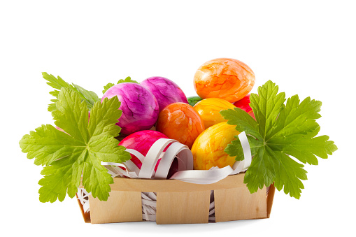 Small basket with painted Easter eggs and geraniums on a white background.