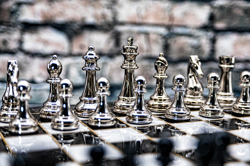 A fully set up chess board with both the black and white pieces set in their squares, shot in studio against a brick background.
