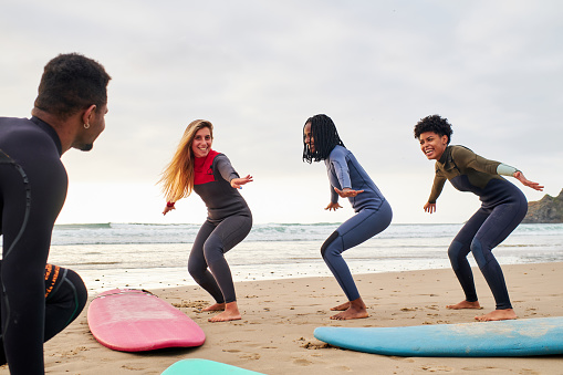 Portrait of confident group of friends practicing how to surf on the sand before entering the sea.