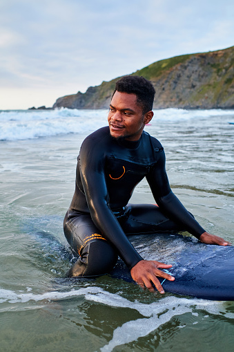 Vertical image of a confident young man sitting on his surfboard inside the sea looking to a side.