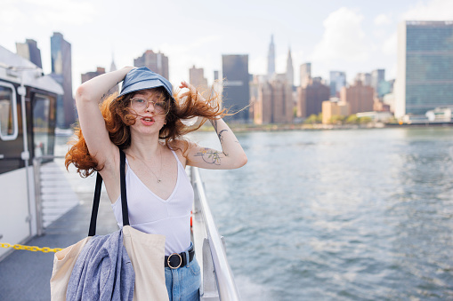 Young woman is talking and holding her hat on a windy day, during ferry ride on East River in New York City.