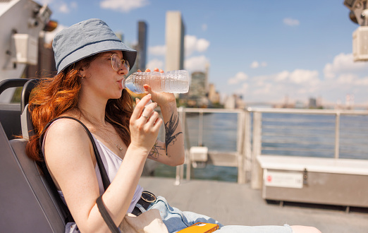 Young woman is refreshing during her ferry ride on East River in NYC, on a hot, summer day.