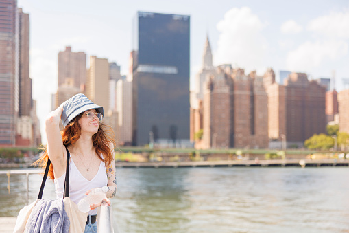 Young woman is riding ferry on East River in New York City, with Manhattan view behind.