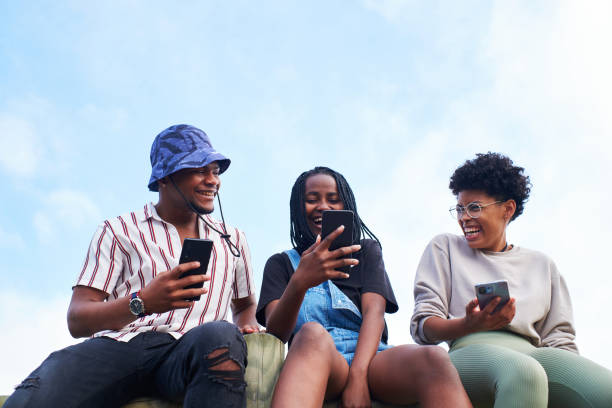 Three friends using their cell phone laughing together outdoors
