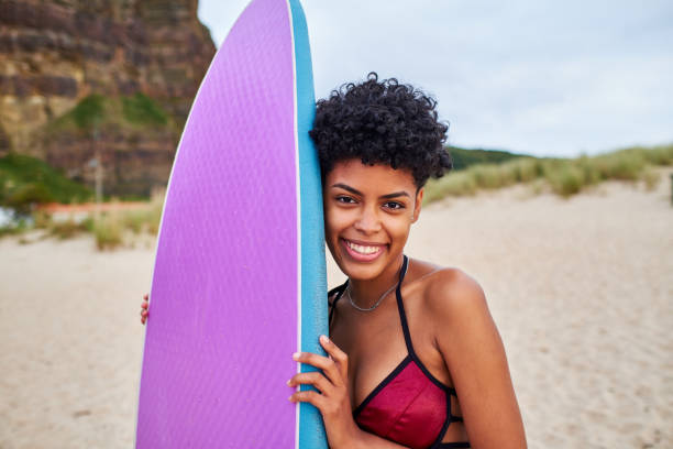 istock Young surfer woman holding her surfboard and looking at camera while smiling on the beach 1479854564