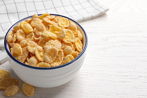 Bowl of tasty corn flakes on white wooden table. Space for text