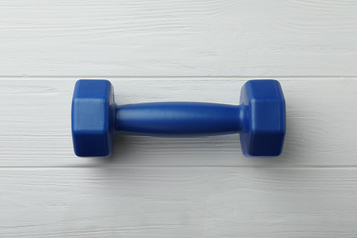 One blue dumbbell on white wooden table, top view