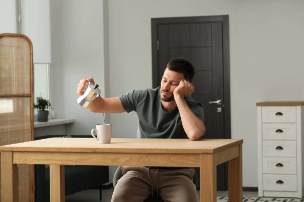 屋内の木製のテーブルでカップにコーヒーを注ぐ眠そうな男 - cup coffee pot coffee coffee cup ストックフォトと画像