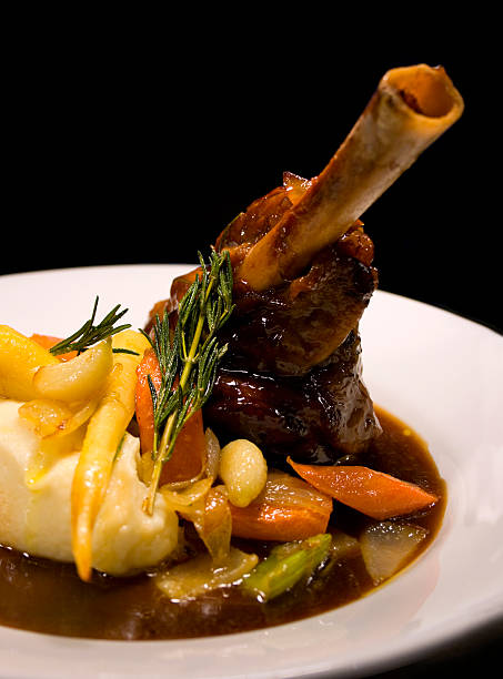 Lamb Shank Lamb shank with seasonal vegetables and gravy on a a black background beautifully prepared by the chef braised stock pictures, royalty-free photos & images