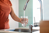 Unrecognizable Woman Filling Glass With Water From Tap In Kitchen