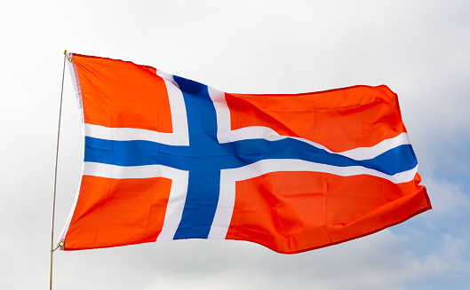 Norwegian flag flies proudly in wind against blue sky
