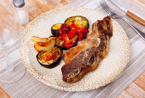 Photo of on blue plate-grilled beef ribs with fried vegetables-aubergine, pepper,onion