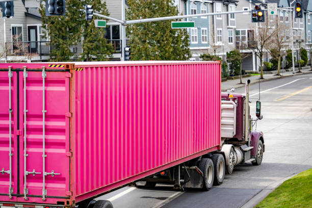 Classic big rig day cab semi truck tractor transporting bright pink container on semi trailer driving on the urban city street