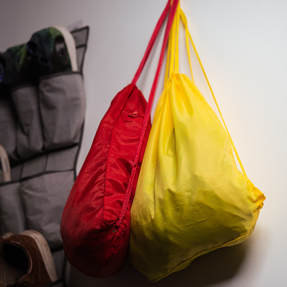 Two sport bags hanged next to a window, next to a hiking backpack and shoes for different ocassions.