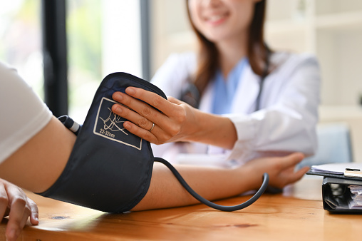 Close-up image of an Asian female doctor checking patient's pulse, heart rate and blood pressure with a monitor in the examination room. Medical and health care concept