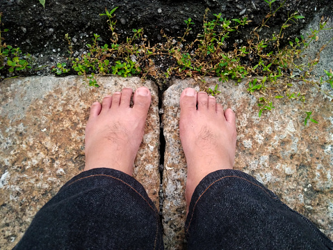 Penang, Malaysia. \n\nThis batch contains photos of granite slab as background.\nSome photos show a man's barefeet and some showing those feet in socks and blue sandals. Some show the man's feet on upper slab and some on lower slab. The black bit on top portion of photo is tar road.