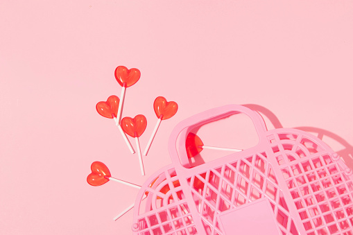 Summer creative layout pink jelly basket and heart lollipops on pastel pink background. 80s or 90s retro fashion aesthetic love concept. Minimal romantic cosmetic idea.