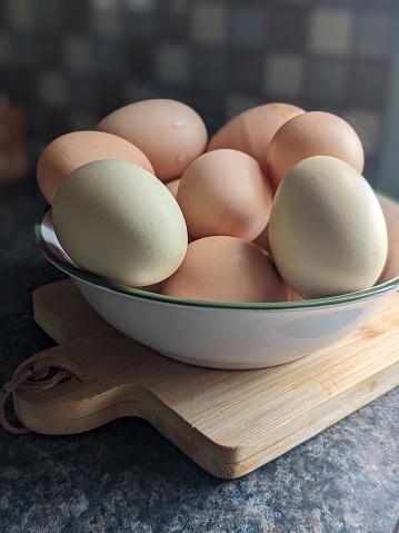 A bowl of eggs straight from the coop sitting on a cutting board in a kitchen