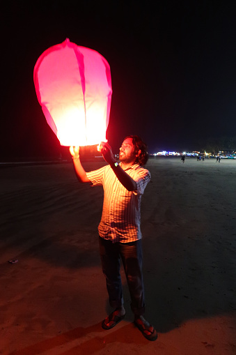 Stock photo showing close-up view of illuminated, Chinese paper lantern being released on beach by the sea at night.
