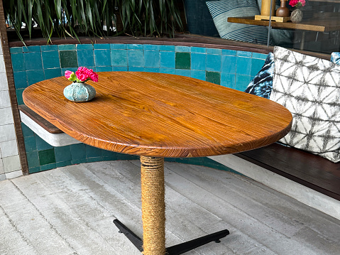 Stock photo showing a wooden pedestal table with bench seating at restaurant or bar, polished wood in a public food and drink establishment with nobody sitting in this cafe, a glossy blue tiled wallcan be found next to the bench