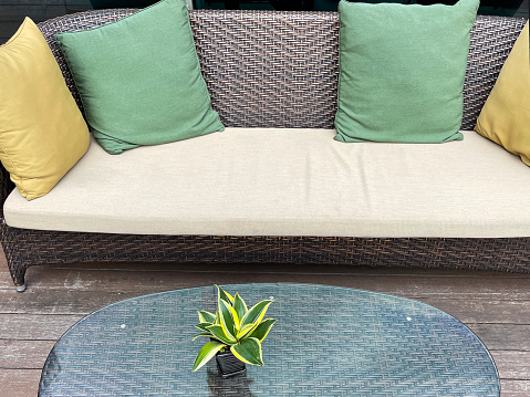 Stock photo showing a set of rattan wicker garden furniture, these robust outdoor chairs are waterproof and make for excellent barbecue and balcony furniture, dark coloured weaved alfresco seating with yellow and greencushions