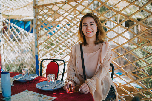Asian Chinese female tourist sitting in restaurant patio looking at camera smiling in Tinghir, Morocco