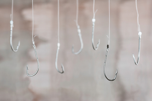 Fishing hooks are hanging with transparent string in front of brown background.