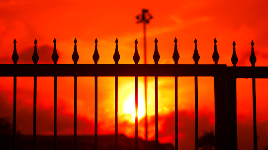 silhouette photo of an iron fence with pointed ends against the background of the evening sky and bright sunsets.