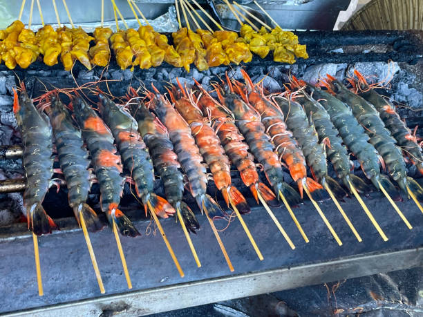 istock Close-up image of uncooked chicken kebabs, marinated raw chicken breast pieces on bamboo skewers, chargrilled prawns lying in rows over hot charcoal embers, elevated view, focus on foreground 1479966213