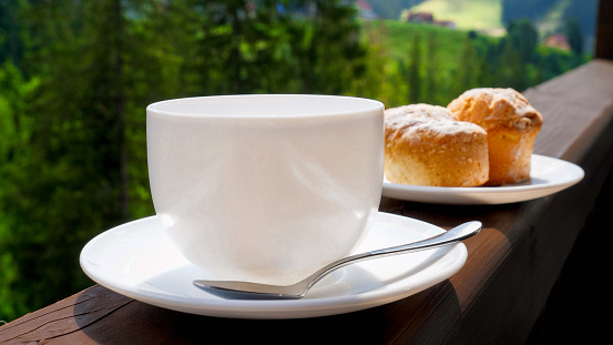 Cup of coffee and muffins on breakfast on the wooden balcony at mountain hotel. Concept of people traveling, tourism and vacation in mountains at summer