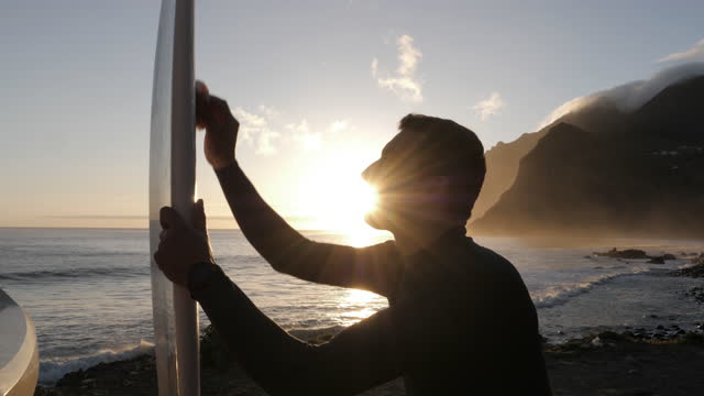 Surfer waxing his surfboard on the beach at sunrise.