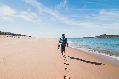 Mochilero apasionado, mochila y botas en mano, camina por la playa Praia da Ilha do Pessegueiro en el Océano Atlántico cerca de Porto Covo, Portugal. Tras los pasos de Rota Vicentina photo