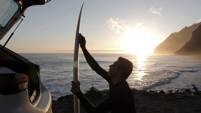 Surfer waxing his surfboard on the beach at sunrise.