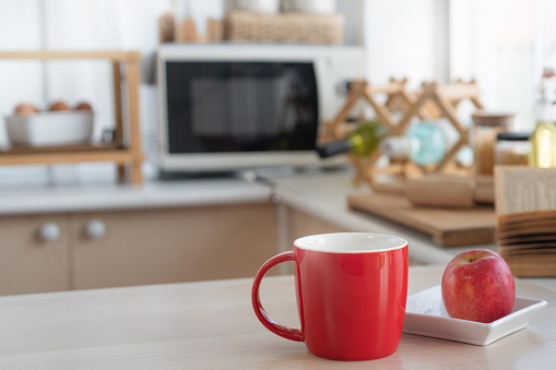 Red cup and red apple on plate on table in modern kitchen