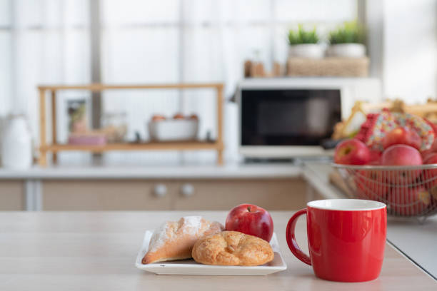 Red cup with croissants and apple on plate, on table in modern kitchen