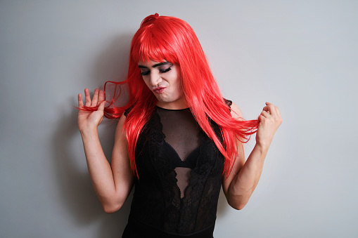 Portrait of drag queen wearing a red wig on grey background. LGBTQ queer.