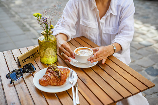 A woman has reserved a table for breakfast on the cafe's summer terrace. a crispy croissant with coffee