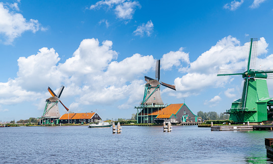 Colorful traditional Dutch windmills along Zaan river. Blue sky with fluffy clouds on the background.