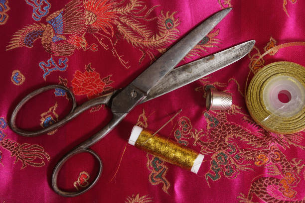 istock Spool of Gold Thread and Thimble on Vintage Asian Pink Silk Fabric 1479989430