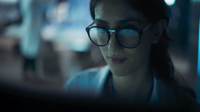Portrait of Beautiful Multiethnic Woman Working on Computer with the Screen Reflecting in Her Glasses. Young Intelligent Female Scientist Working in Laboratory. Background with Technological Lights